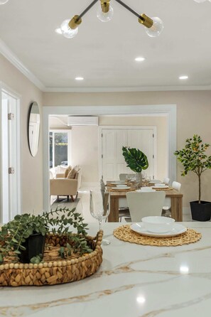 A dining area with a wooden table, white chairs, a potted plant, and a marble countertop.