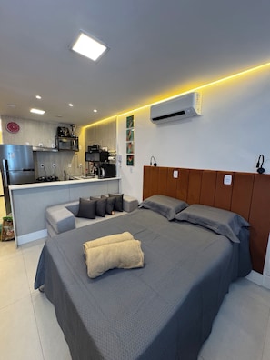 A modern bedroom with a bed, bedside tables, a built-in desk, and a kitchenette. - Copacabana SKY View (Rio de Janeiro)