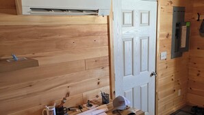 A wooden-paneled room with a desk, a white door, and a wall-mounted electrical panel. - Cozy 1-bedroom private cabin  with AC and heat. Minutes to Sacanadaga Lake (Broadalbin)