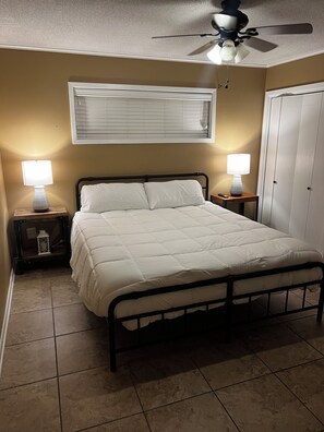 A bedroom with a bed, two bedside lamps, a ceiling fan, and a window with blinds.