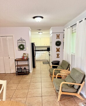 A living room with a sofa, chairs, a coffee table, and a kitchen in the background. - Southern Charm- pets allowed! 2 miles from Casinos (Lake Charles)