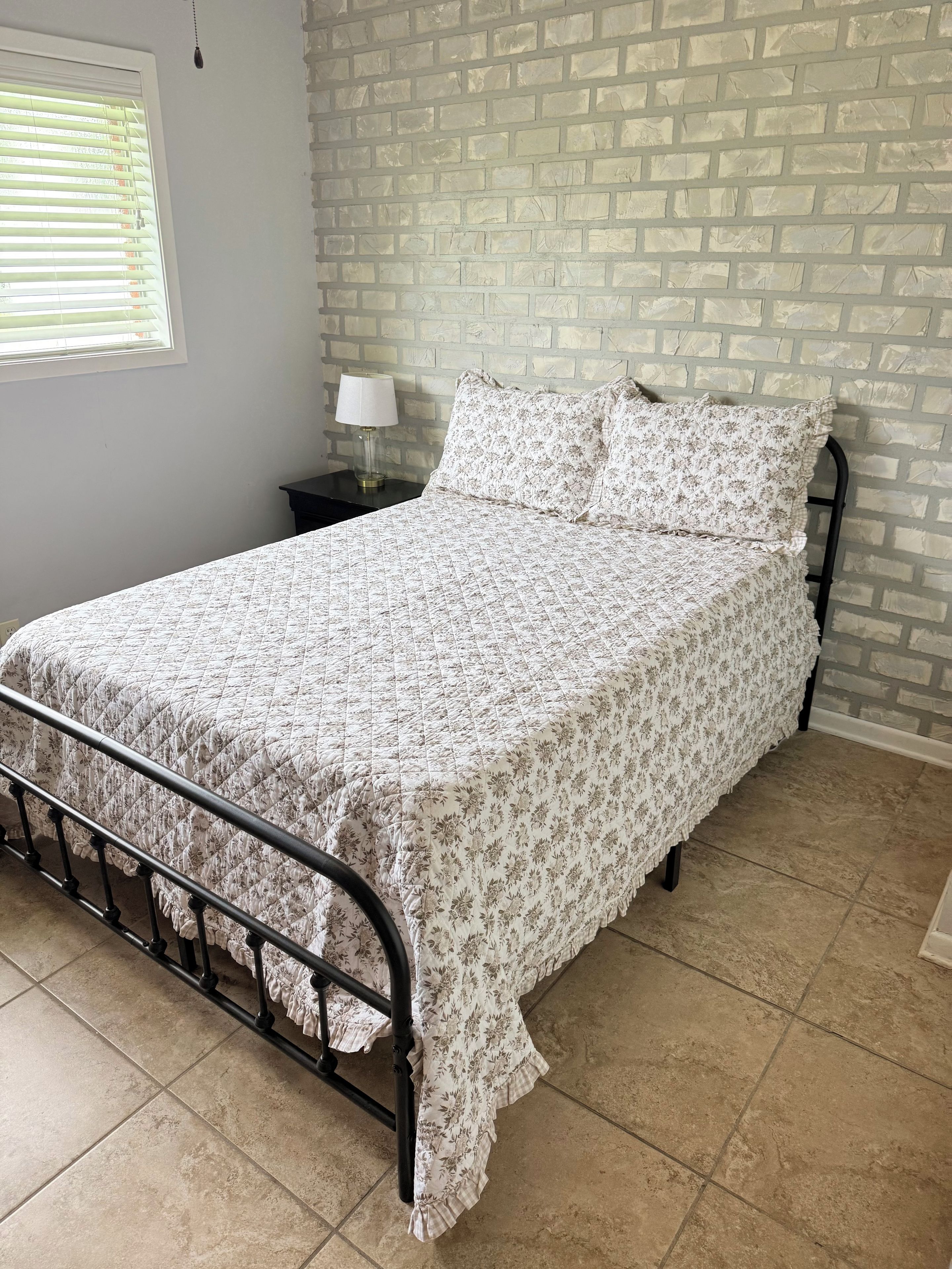 A bed with a floral bedspread, a nightstand with a lamp, and a brick-patterned wall.