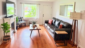 Ein Wohnzimmer mit Kamin, Fernseher, einer Couch, einem Couchtisch und einem großen Spiegel.