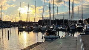 Una marina con diverse barche a vela ormeggiate, un viale lastricato e un tramonto sullo sfondo.