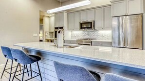 A modern kitchen with a central island, bar stools, stainless steel appliances, and a bright overhead light. - Eagle Crest Golf Resort Amenities on the 17th Tee (Redmond)