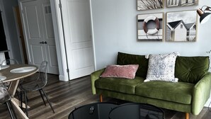 A living room with a green sofa, a coffee table, and a dining area with chairs and a table.