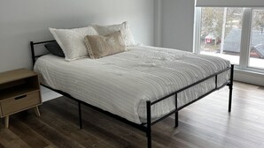 A modern bedroom with a bed, a nightstand, and a large window.