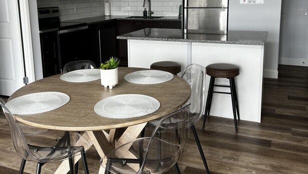A modern kitchen with a central island, a dining area with a round table and chairs, and a hanging light fixture.