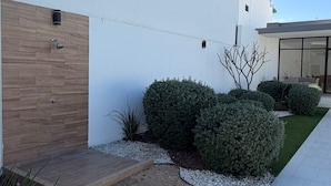 A modern building with a wooden door, a small garden with shrubs, and a white exterior wall. - Modern house with 3 bedrooms, pool, La Paz BCS (La Paz)