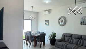 A modern living room with a gray sofa, a dining table with chairs, a potted plant, and a unique ceiling light fixture. - Modern house with 3 bedrooms, pool, La Paz BCS (La Paz)