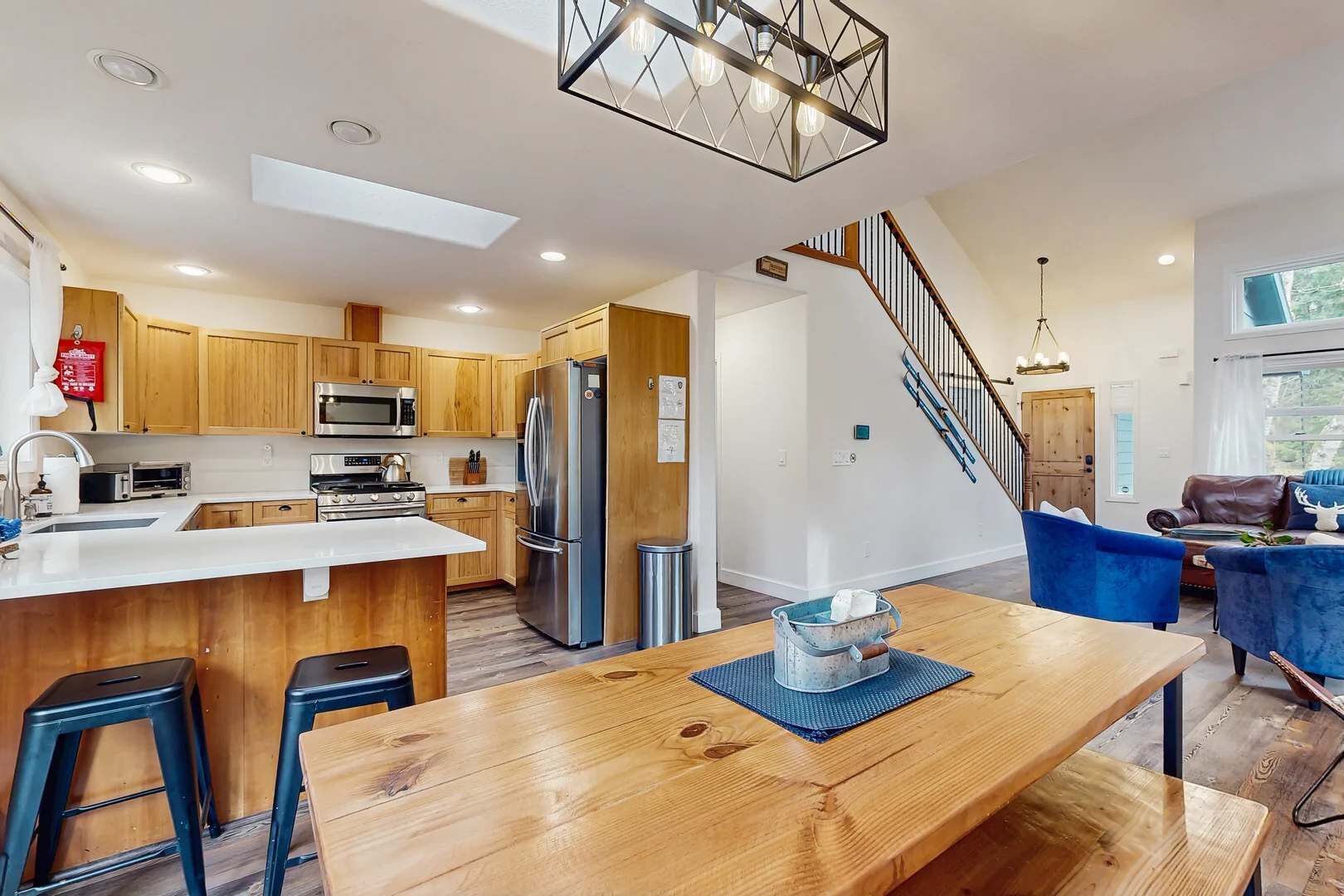 Una cocina moderna con electrodomésticos de acero inoxidable, una isla de madera y un comedor con mesa de madera y sillas azules.
