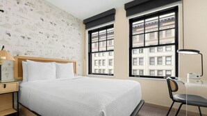 A neatly arranged hotel room with a bed, desk, chair, and large windows. - FOUND Hotels, San Diego Downtown, Series by Marriott  (San Diego)