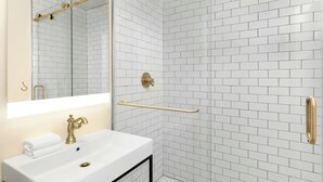 A bathroom with a white sink, gold fixtures, a glass shower enclosure, and a tiled wall. - FOUND Hotels, San Diego Downtown, Series by Marriott  (San Diego)