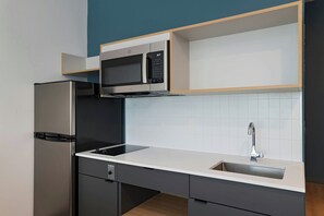 Una cocina moderna con microondas integrado, refrigerador de acero inoxidable y un lavamanos con grifo.