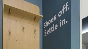 Un zapatero de pared con ganchos, una mesita y una pared con un mensaje.