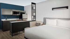 A modern hotel room with a bed, a desk, a microwave, and a small kitchenette. - StudioRes by Marriott Louisville East (Louisville)