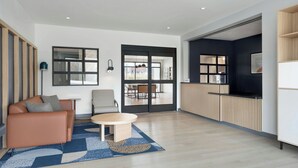 A modern living room with a sofa, a round table, and a view through a glass door to an outdoor area. - StudioRes by Marriott Louisville East (Louisville)