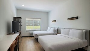 Habitación de hotel con dos camas, un escritorio con televisor, una ventana con persianas y una lámpara fijada a la pared.