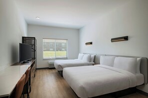 Habitación de hotel con dos camas, un escritorio con televisor, una ventana con persianas y una lámpara fijada a la pared.
