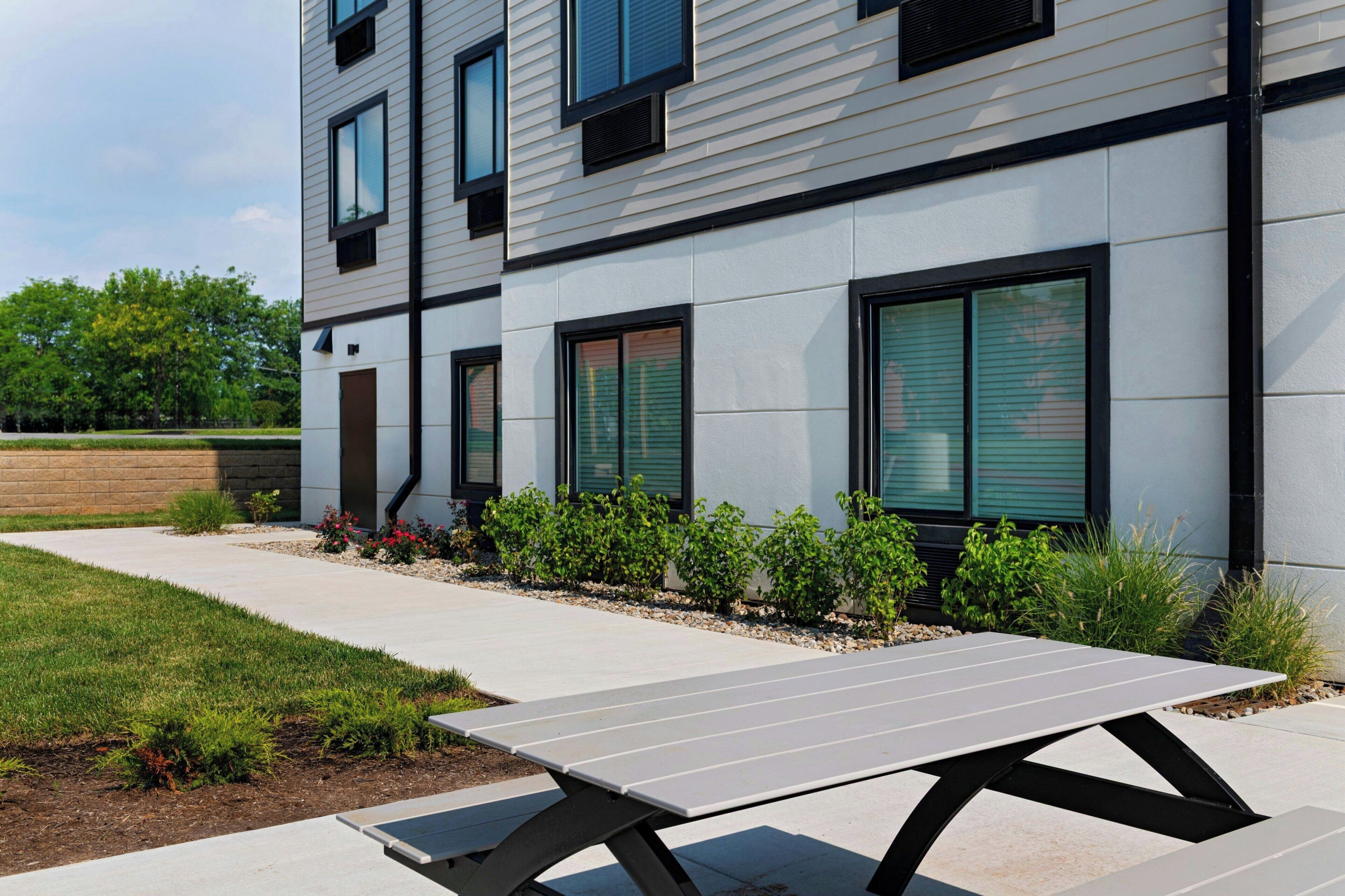 A modern building with a flat roof, large windows, and a paved outdoor area with a picnic table.