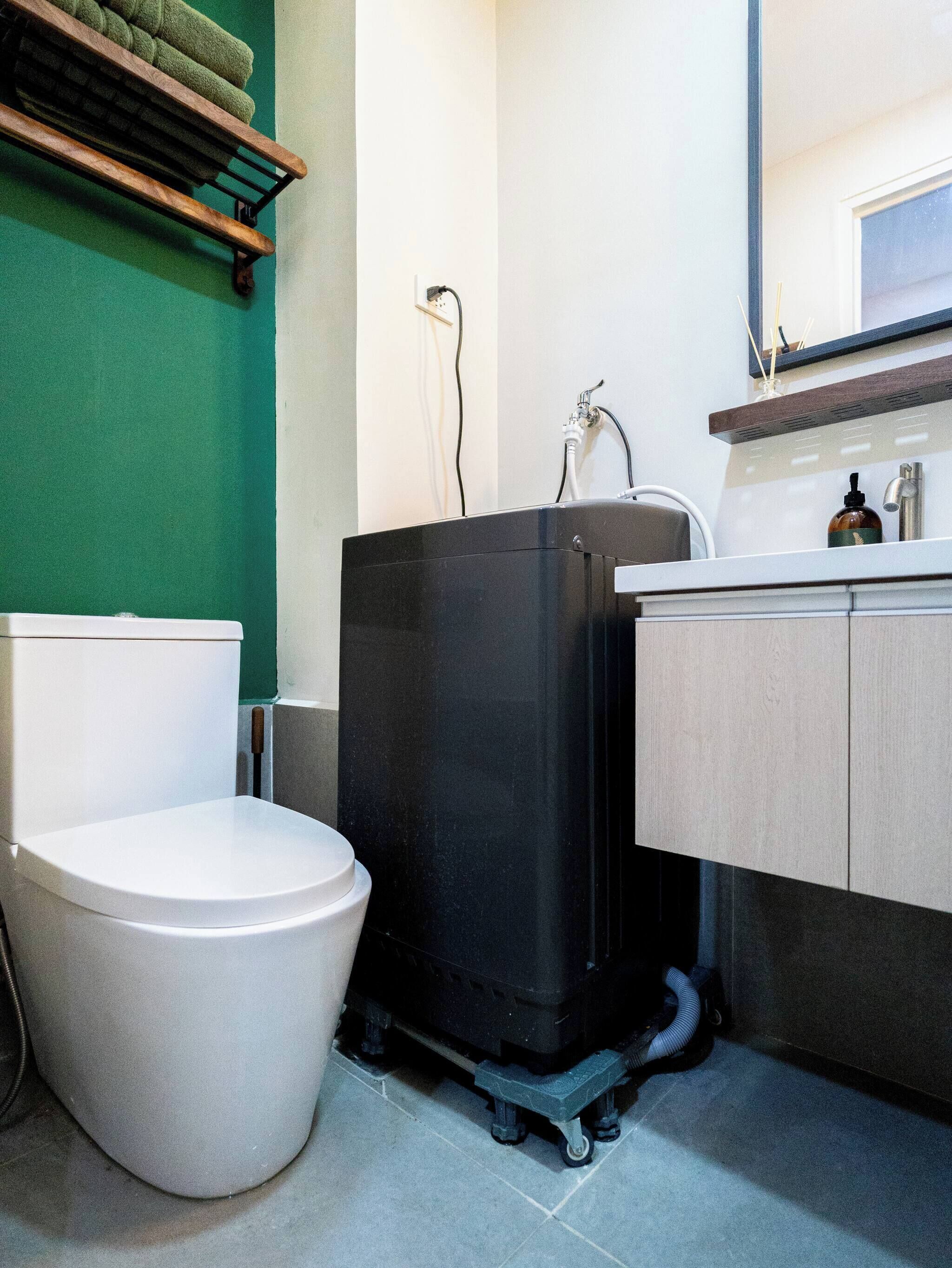 Un baño con inodoro, un carrito de limpieza negro, un lavabo y un espejo.