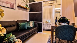 Una sala de estar moderna con un sofá de cuero negro, cojines verdes, una mesa de centro de madera y un comedor con mesa y sillas.