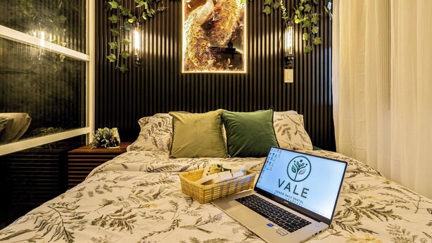 Un dormitorio con cama, computadora portátil, decoración de pavo real en la pared y ventana con vistas.