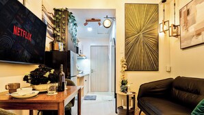 Una sala moderna con televisor, comedor, sofá de cuero negro y un adorno en la pared.