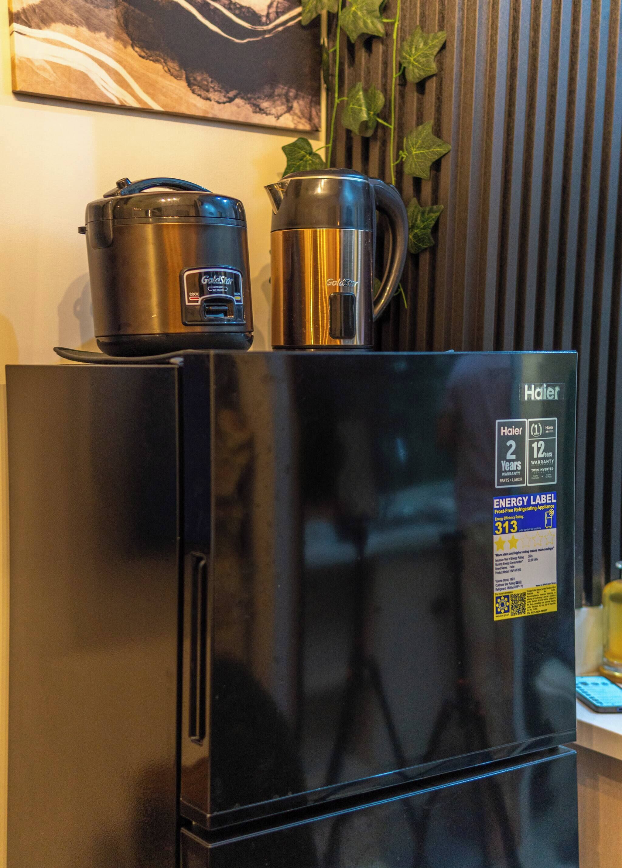 A black Haier refrigerator with a digital display, a stainless steel pot, and a kettle on top.
