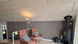 A modern living room with two leather armchairs, a round table, a floor lamp, a wood-burning stove, and a striped wall. - Holiday home near forest and beach (Egernsund)