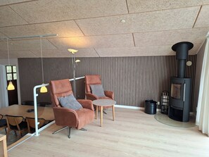A modern living room with two leather armchairs, a round table, a floor lamp, a wood-burning stove, and a striped wall. - Holiday home near forest and beach (Egernsund)