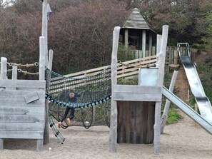 Ein Spielplatz mit einer Seilbrücke, einer Holzer Rutsche und einer kleinen Schutzhütte.