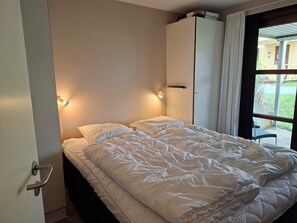A bedroom with a bed, two bedside lamps, a wardrobe, and a window with curtains. - Holiday home near forest and beach (Egernsund)