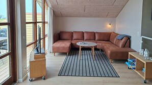 A modern living room with a brown leather sectional sofa, a small round table, a patterned rug, and a wooden side table with a lamp. - Holiday home near forest and beach (Egernsund)