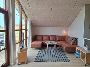 A modern living room with a brown leather sectional sofa, a small round table, a patterned rug, and a wooden side table with a lamp. - Holiday home near forest and beach (Egernsund)