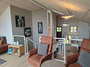A spacious living area with a high ceiling, a glass railing, and a modern pendant light. - Holiday home near forest and beach (Egernsund)