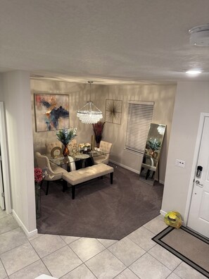 A living room with a sofa, a glass coffee table, a chandelier, and a dining area with chairs and a table. - Modern 3BR Home w/ Open Floor Plan, Huge Yard & Security System – Move-In Ready (Ruskin)