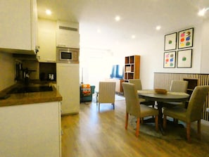 Eine kompakte Küche mit Mikrowelle, ein Essbereich mit Tisch und Stühlen und ein Fernseher im Hintergrund.
