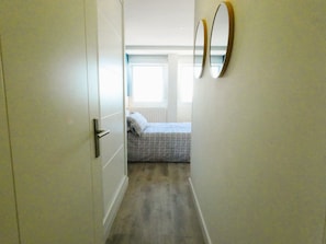 Ein schmaler Flur, der in ein Schlafzimmer mit einem Bett, einer Tür und zwei Wandspiegeln führt.