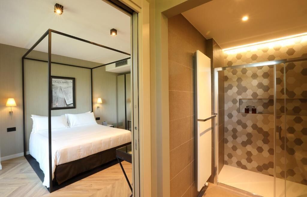 Quarto com cama de dossel, chuveiro com padrão de azulejos hexagonais e espelho fixado na parede.