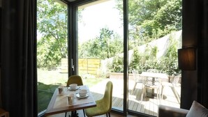 Et værelse med en stor skydedør, der fører ud til en udendørs terrasse med et bord og stole.