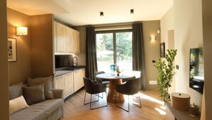 En moderne stue med sofa, spisebord, stole, et køkkenområde og et stort vindue med gardiner.
