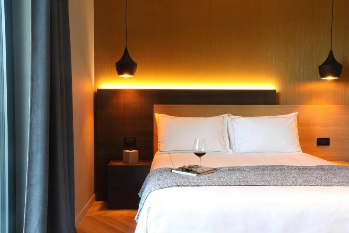 Une chambre d’hôtel avec un lit, une table de chevet et deux lampes suspendues.