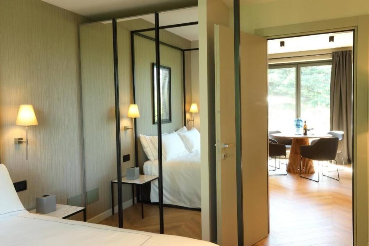 Une chambre d’hôtel comprenant un lit, une table de chevet, une lampe et donnant sur un espace repas avec une table et des chaises.