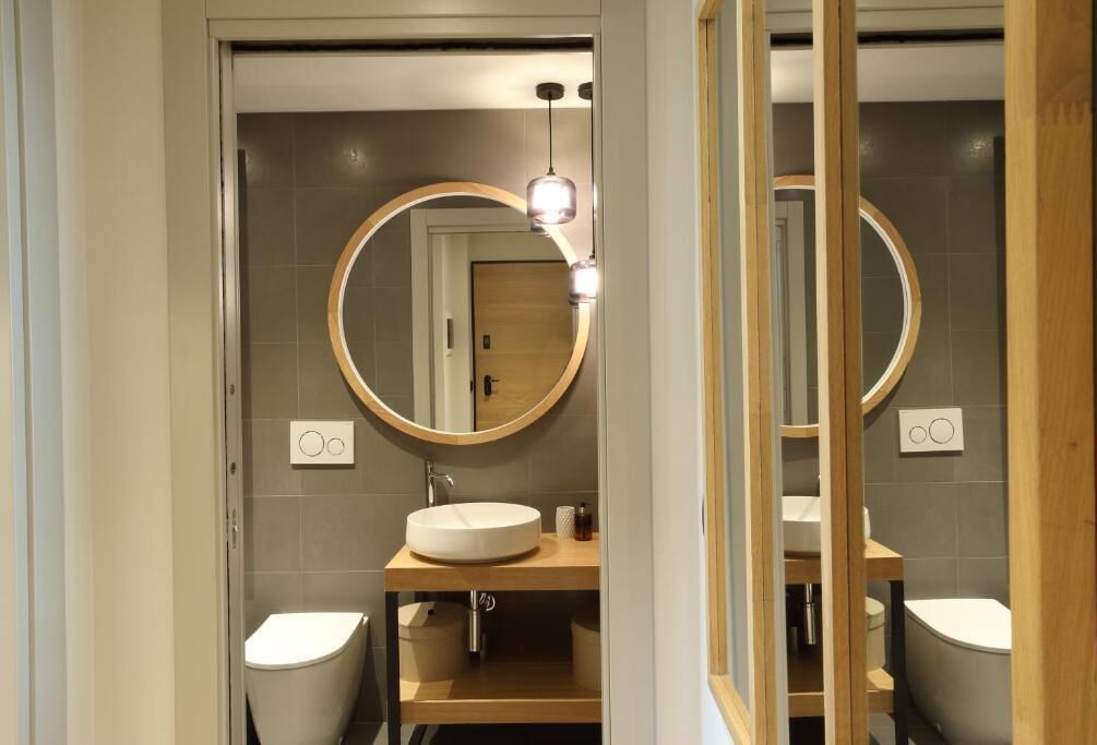 Une salle de bain moderne avec un miroir rond, un lavabo blanc et des toilettes.