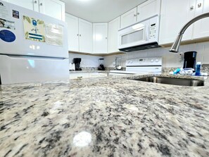 A kitchen with white cabinets, a granite countertop, a stainless steel sink, a microwave, and a stove. - Perdido Dunes 27 Beach Side Orange Beach (Orange Beach)