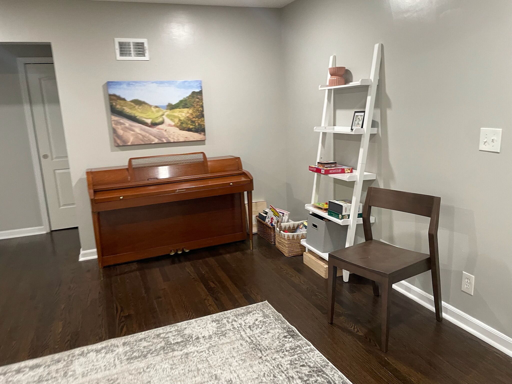 Ein Zimmer mit Klavier, Bücherregal, Sessel und Teppich.
