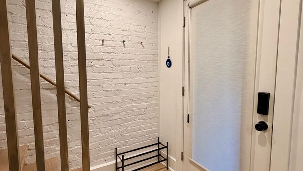 A staircase with wooden railings, a white brick wall, a door with a handle, and a small metal rack. - Light-Filled Lower Suite · Brand New · Private · 5 Mins to Metro · Parking (Washington)