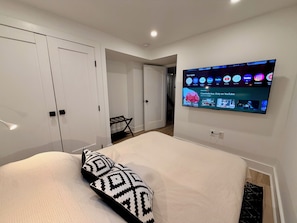A bedroom with a bed, a TV mounted on the wall, a wardrobe, and a small table with a chair. - Light-Filled Lower Suite · Brand New · Private · 5 Mins to Metro · Parking (Washington)