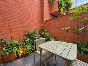 A small outdoor seating area with a table and chairs, surrounded by potted plants and a brick wall. - EMA Condesa (Mexico City)